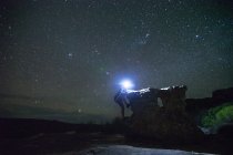 Caminhante do sexo masculino escalando uma rocha no campo à noite — Fotografia de Stock