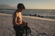Мужчина-серфер держит ремни безопасности на пляже в сумерках — стоковое фото