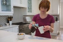 Woman pouring coffee into mug in kitchen at home — Stock Photo
