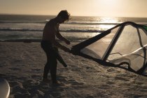 Surfista masculino preparando uma pipa em uma praia ao entardecer — Fotografia de Stock