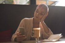 Стильна жінка використовує мобільний телефон, маючи шоколадний молочний торт в ресторані — стокове фото