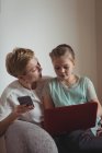 Mother and daughter using mobile phone and laptop in living room art home — Stock Photo