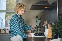 Молода жінка вливає каву в кухоль вдома — стокове фото