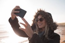 Jeune femme prenant selfie avec téléphone portable à la plage — Photo de stock