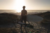 Surfista maschio in piedi con tavola da surf su una spiaggia al crepuscolo — Foto stock