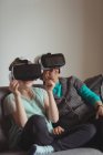 Abuela y nieta usando auriculares de realidad virtual en la sala de estar en casa - foto de stock