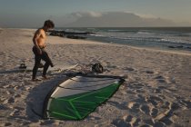 Surfista masculino de pé com pipa e prancha na praia ao entardecer — Fotografia de Stock