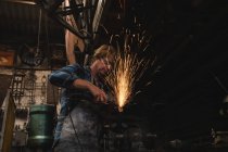 Blacksmith grinding a metal rod with grinder machine n workshop — Stock Photo