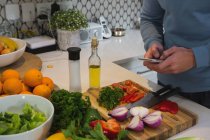 Чоловік використовує мобільний телефон під час різання овочів на кухні вдома — стокове фото