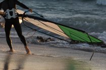 Surfista maschio che tiene un aquilone sulla spiaggia al crepuscolo — Foto stock