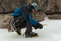 Masculino escalador de rocha vestindo crampons perto de montanha rochosa durante o inverno — Fotografia de Stock