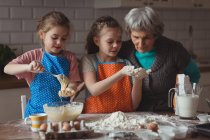 Abuela y nietas preparando magdalena en la cocina en casa - foto de stock