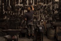 Blacksmith looking at metal equipment in workshop — Stock Photo