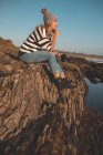 Задумчивая женщина, сидящая на скале на пляже — стоковое фото