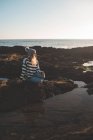 Задумчивая женщина, сидящая на скале на пляже — стоковое фото