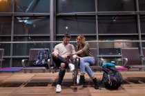 Casal usando telefone celular na área de espera no aeroporto — Fotografia de Stock