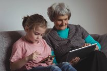 Бабуся і онука використовують цифровий планшет і мобільний телефон у вітальні вдома — стокове фото
