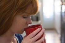 Mulher tomando café em caneca vermelha em casa — Fotografia de Stock