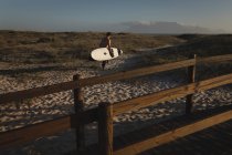Surfista di sesso maschile che cammina con tavola da surf su una spiaggia — Foto stock