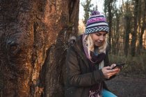 Молодая женщина использует мобильный телефон в лесу — стоковое фото
