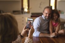 Mother taking photo of father and daughter with mobile phone at home — Stock Photo