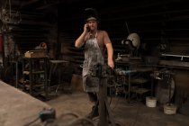 Blacksmith talking on mobile phone in workshop — Stock Photo