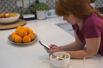 Mujer usando teléfono móvil en la cocina en casa - foto de stock