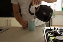 Sezione media dell'uomo versando acqua calda nella tazza a casa — Foto stock