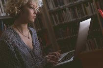 Jovem mulher usando laptop na biblioteca — Fotografia de Stock