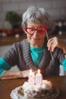 Mujer mayor con pastel de cumpleaños con máscara de mascarada en casa - foto de stock