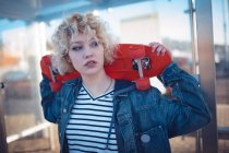 Nachdenkliche Frau hält Skateboard an Bushaltestelle — Stockfoto
