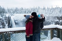 Coppia scattare selfie con telefono cellulare vicino alla cascata durante l'inverno — Foto stock
