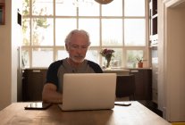 Старший чоловік, використовуючи ноутбук кухні в домашніх умовах — стокове фото