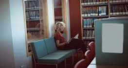 Giovane donna che legge un libro in biblioteca — Foto stock