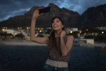 Jeune femme prenant selfie avec téléphone portable à la plage — Photo de stock