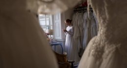 Mariée caucasienne en robe de mariée en utilisant le téléphone mobile dans la boutique — Photo de stock