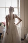 Noiva em vestido branco olhando através da janela na boutique, visão traseira — Fotografia de Stock