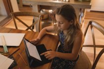 Menina atenta usando tablet digital em casa enquanto sentado à mesa — Fotografia de Stock