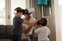 Father helping his son in using virtual reality headset in living room at home — Stock Photo