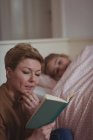 Mãe lendo um livro enquanto menina dormindo no quarto em casa — Fotografia de Stock