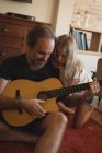 Padre con su hija tocando la guitarra en la sala de estar en casa - foto de stock