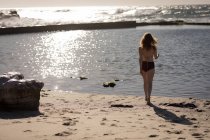 Vista trasera de la mujer en bikini parada cerca de la orilla del mar - foto de stock