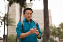 Casual mid adult man with backpack checking phone on city street — Stock Photo