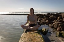 Donna attraente che fa meditazione vicino alla piscina sulla spiaggia in una giornata di sole — Foto stock