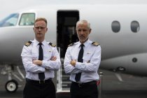 Portrait of two male pilots standing with arms crossed — Stock Photo