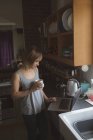 Красива жінка використовує ноутбук, маючи каву на кухні вдома — стокове фото