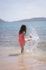 Chica jugando en el agua en la playa en un día soleado - foto de stock