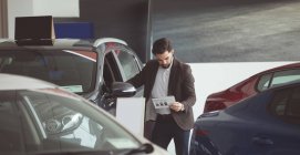 Salesman standing next to car and reading brochure at showroom — Stock Photo