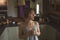 Mulher cuidadosa segurando xícara de café na cozinha em casa — Fotografia de Stock
