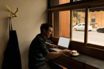 Empresário usando laptop enquanto toma café no café — Fotografia de Stock